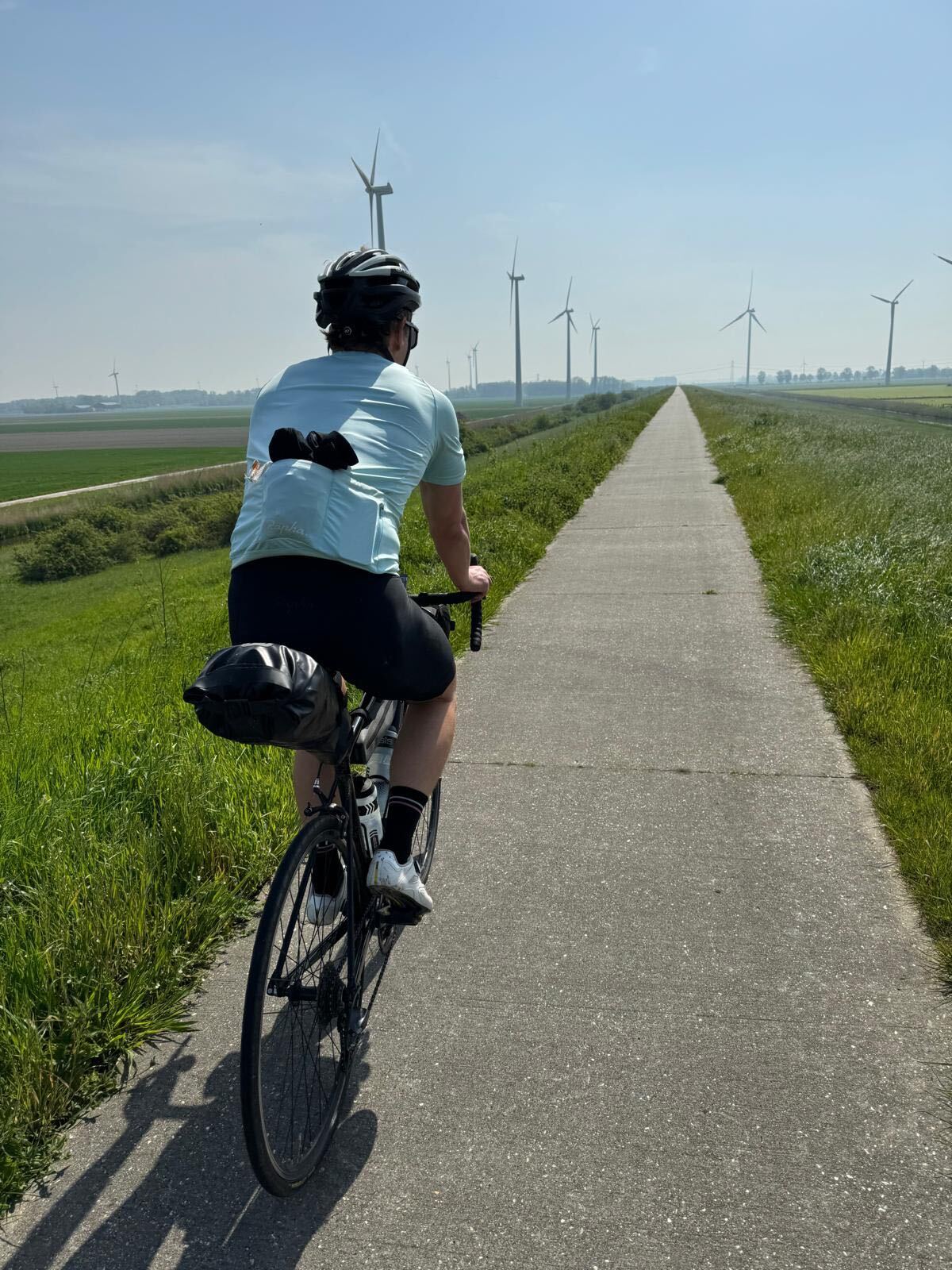 Cyclist on a Dutch polder dyke with wind turbines on the horizon