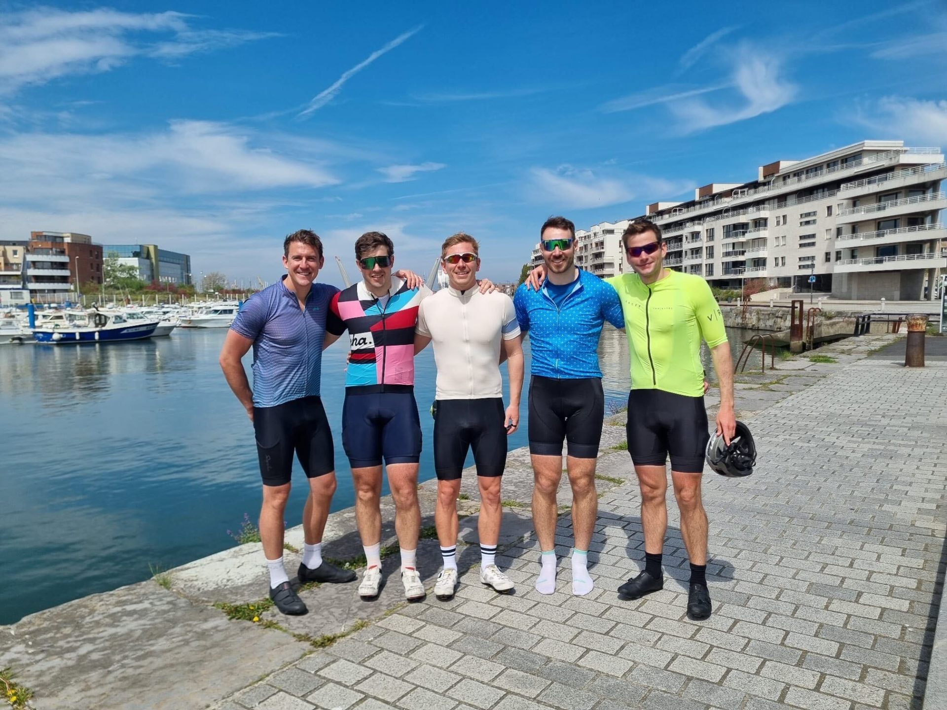 Group of five cyclists posing by a harbour marina