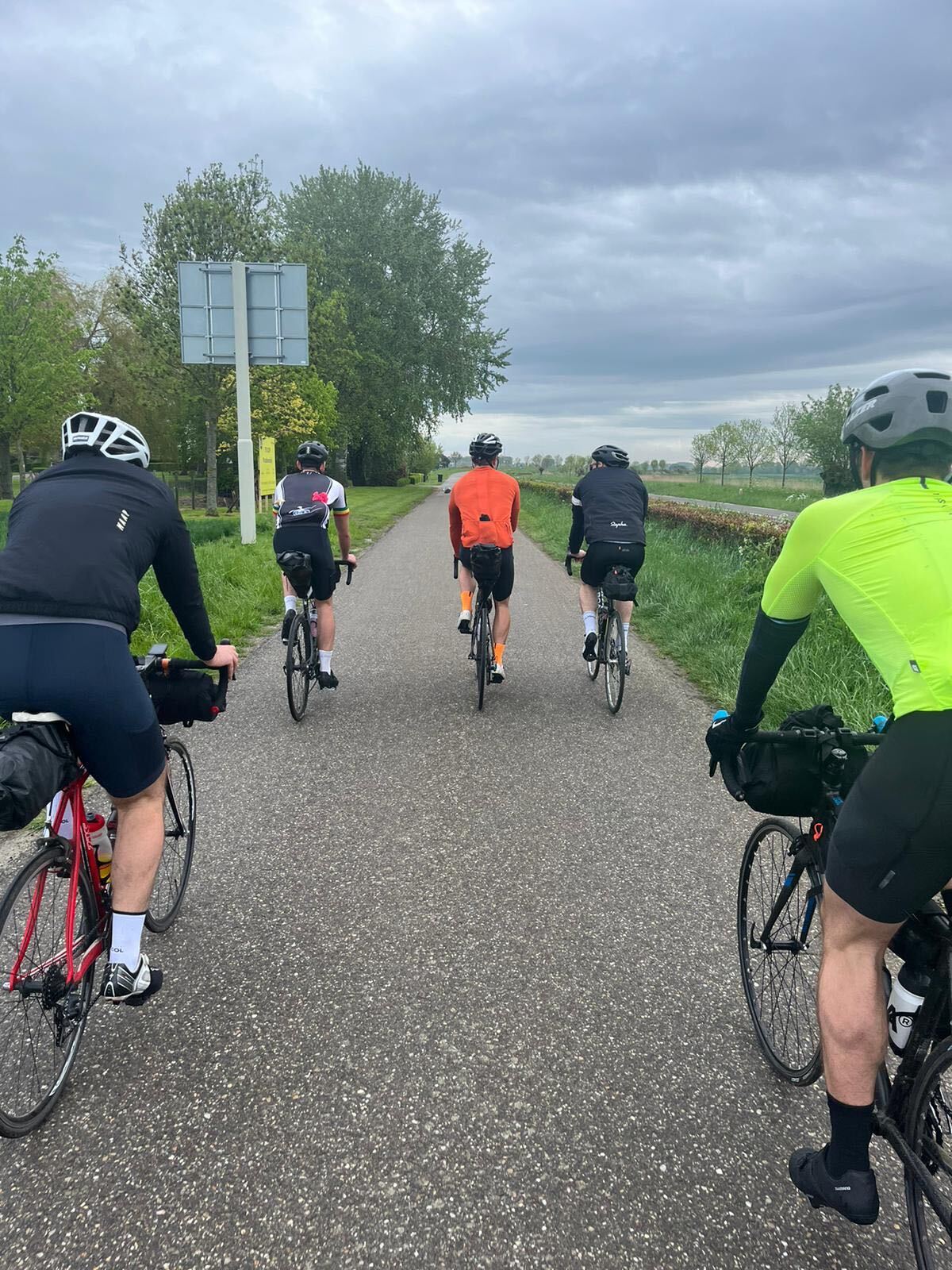 Group riding together along a quiet polder road under cloudy skies