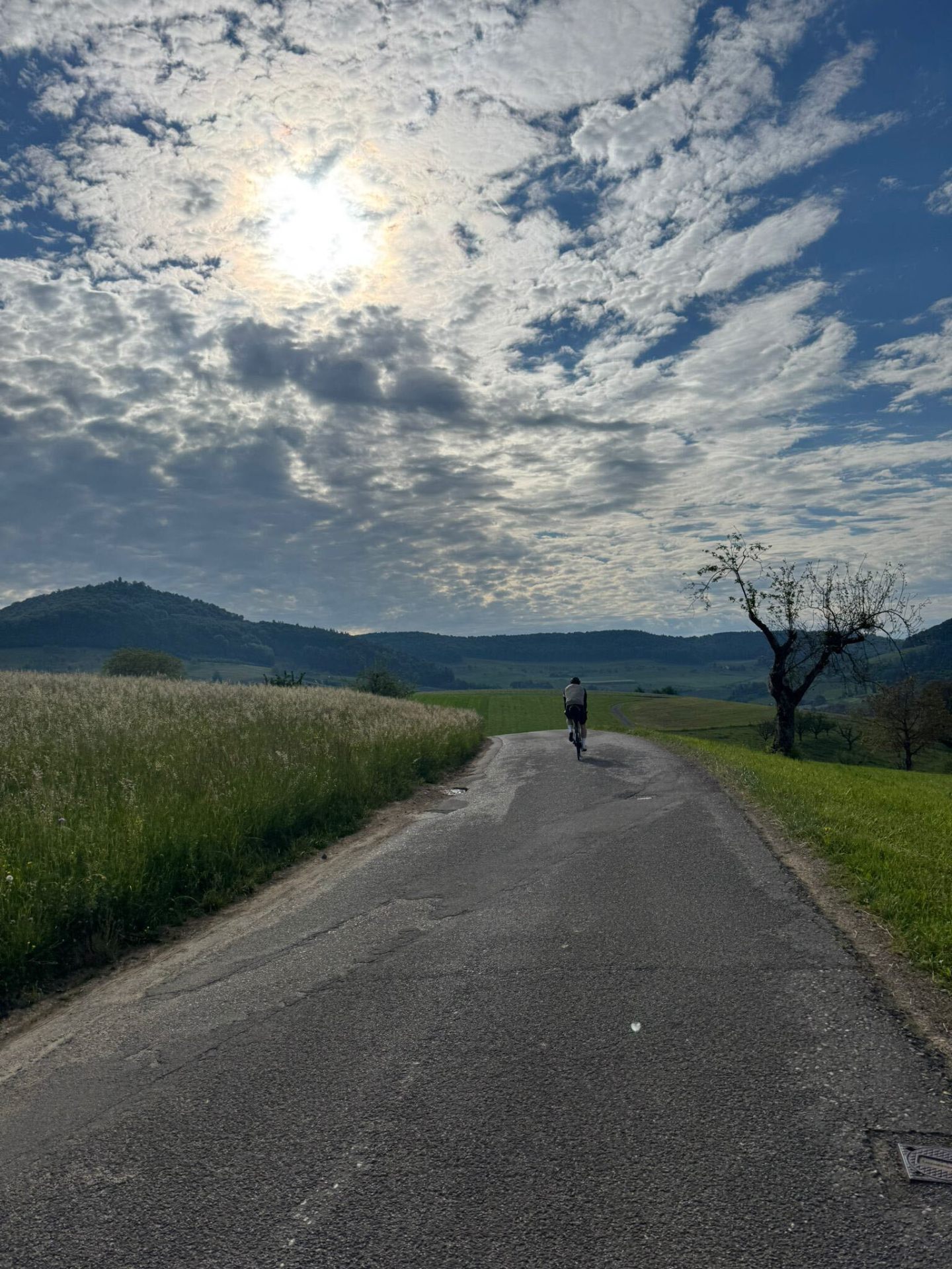Cyclist climbing a quiet road under a dramatic mackerel sky in the Swiss pre-Alps