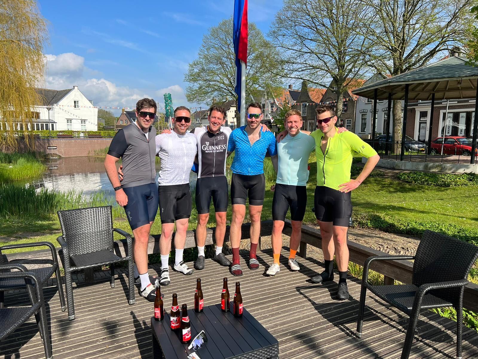 Group of six cyclists posing by a Dutch village square with beers