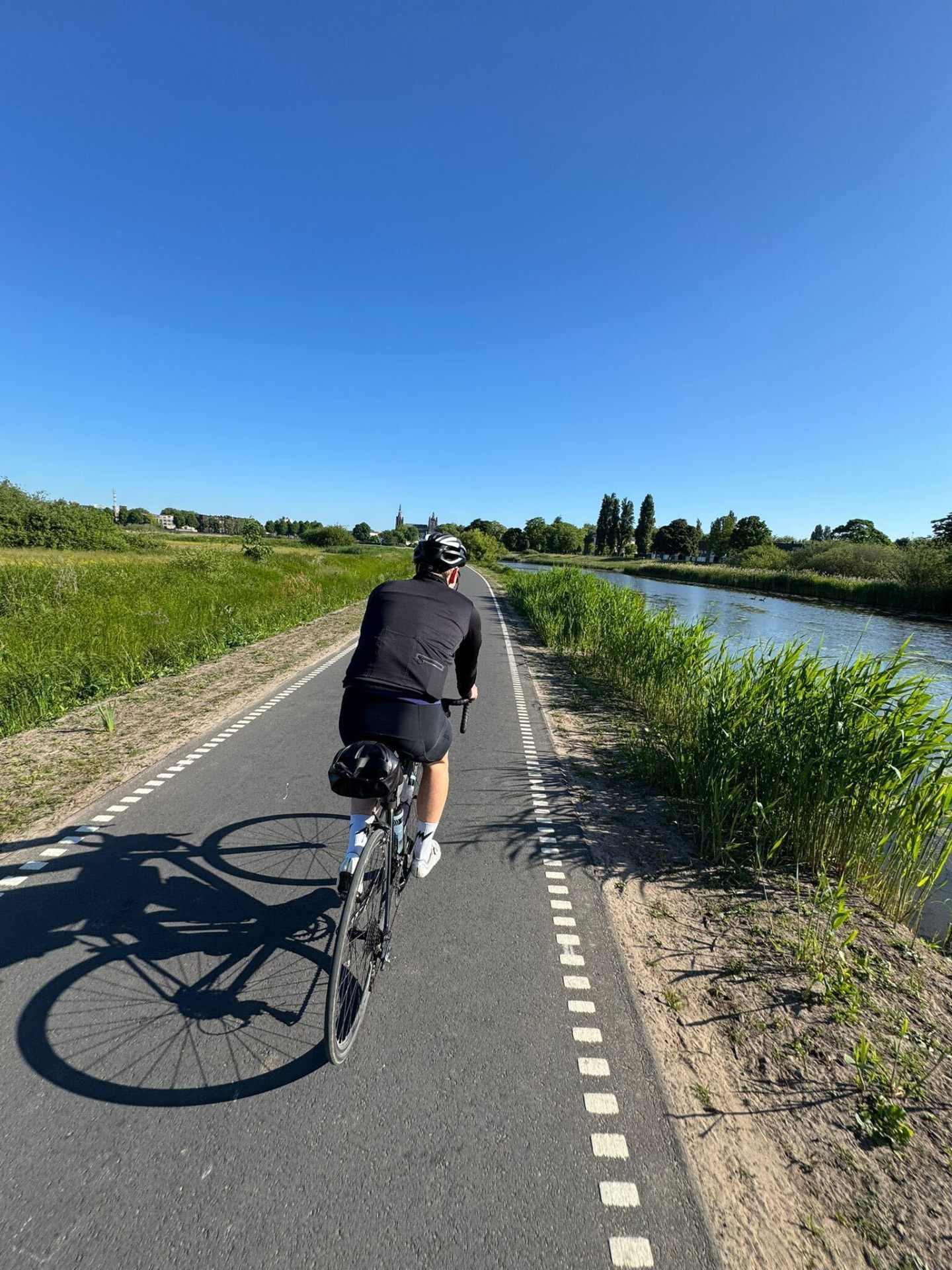 Cyclist on a riverside cycle path approaching a Dutch town
