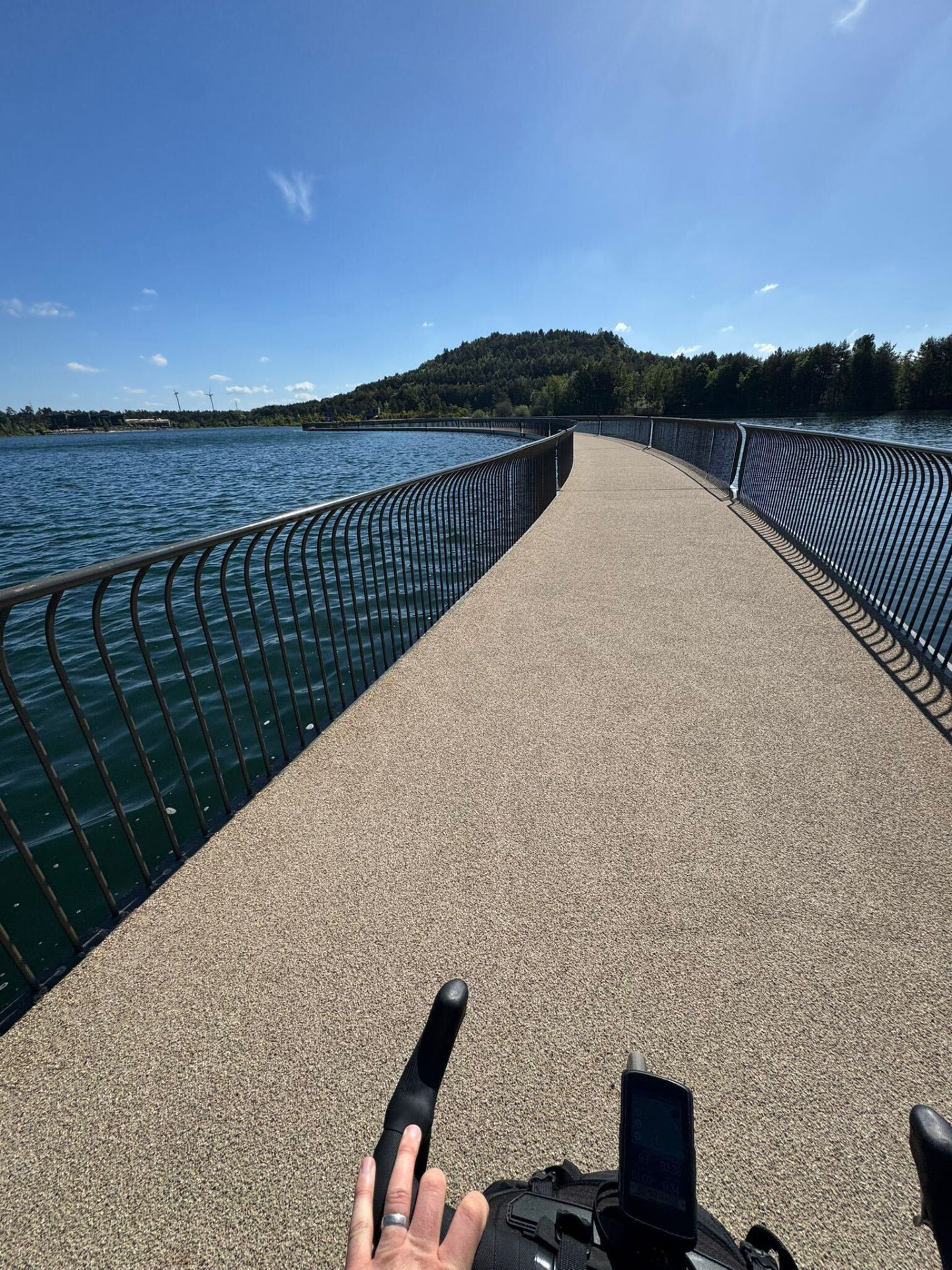 Curved pedestrian and cycle bridge over a lake under a blue sky