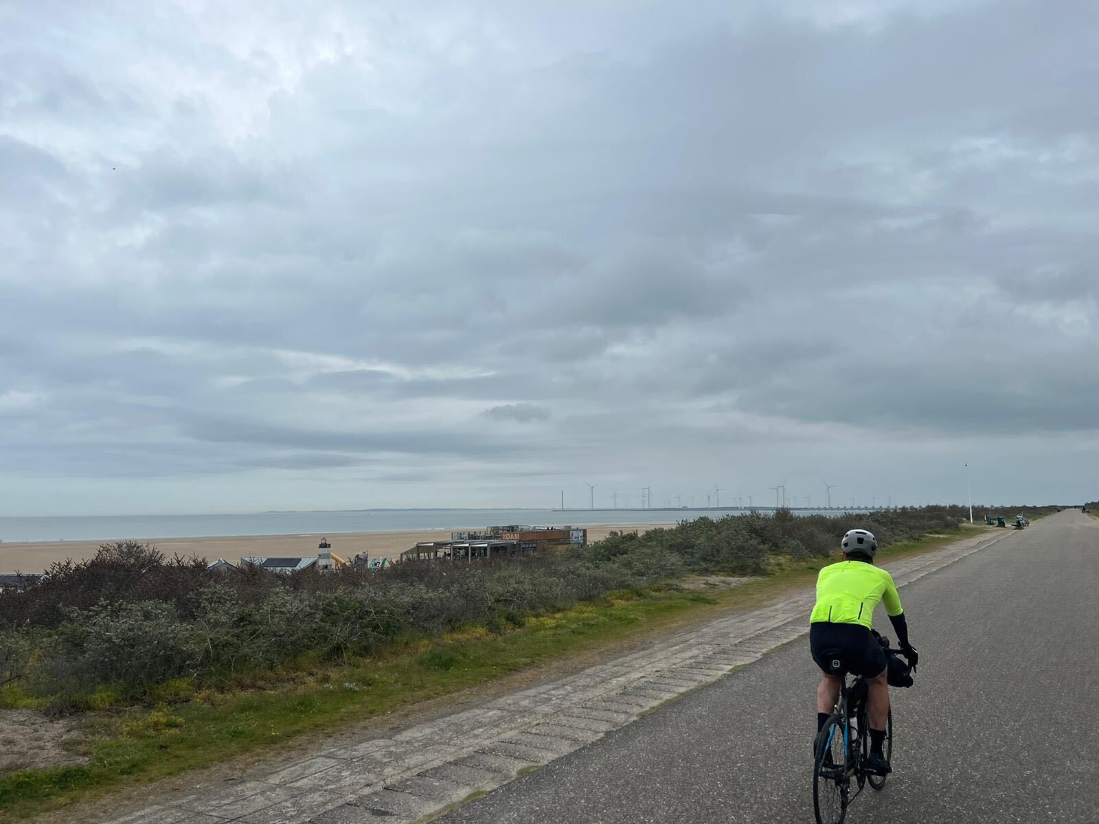 Solo cyclist on a coastal promenade with wind turbines on the horizon